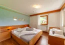 Doppelzimmer mit Holzbett, Zusatzbett und Fensterblick auf grüne Berghänge im Sarntal