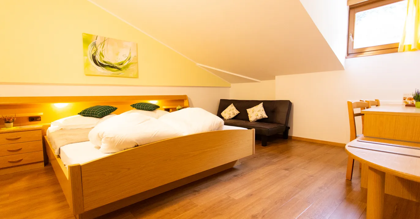 Doppelzimmer mit Holzbett, gelber Wand, Sofa und Sitzecke unter der Dachschräge