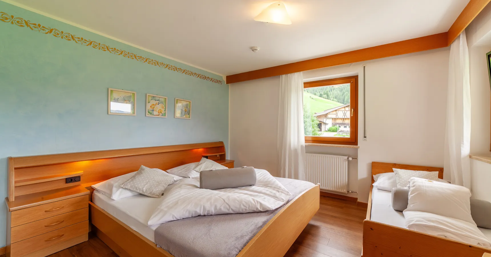 Doppelzimmer mit Holzbett, Zusatzbett und Fensterblick auf grüne Berghänge im Sarntal