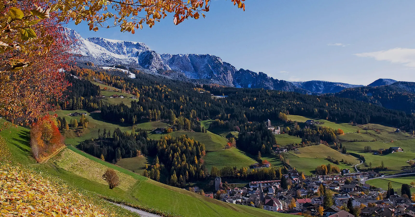 Herbstliches Dorf im Tal mit buntem Laub und schneebedeckten Bergen, malerisches Panorama