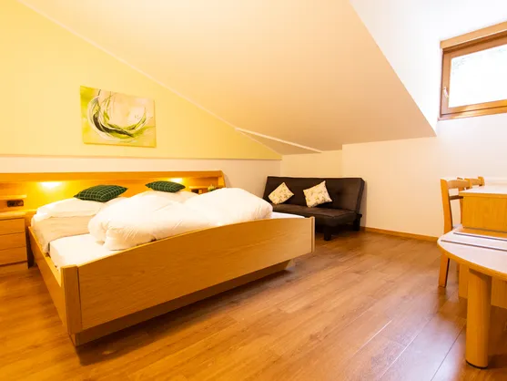 Doppelzimmer mit Holzbett, gelber Wand, Sofa und Sitzecke unter der Dachschräge