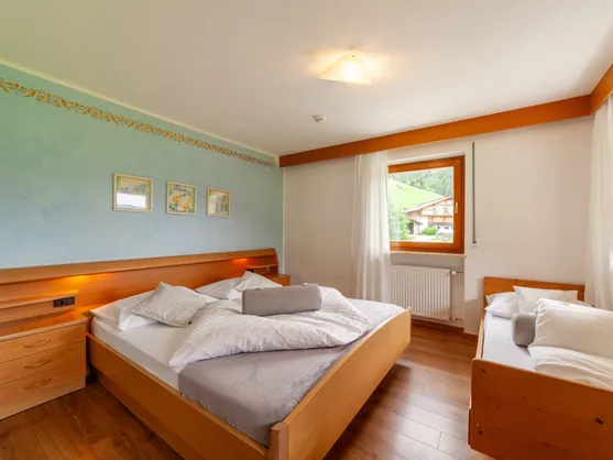 Doppelzimmer mit Holzbett, Zusatzbett und Fensterblick auf grüne Berghänge im Sarntal
