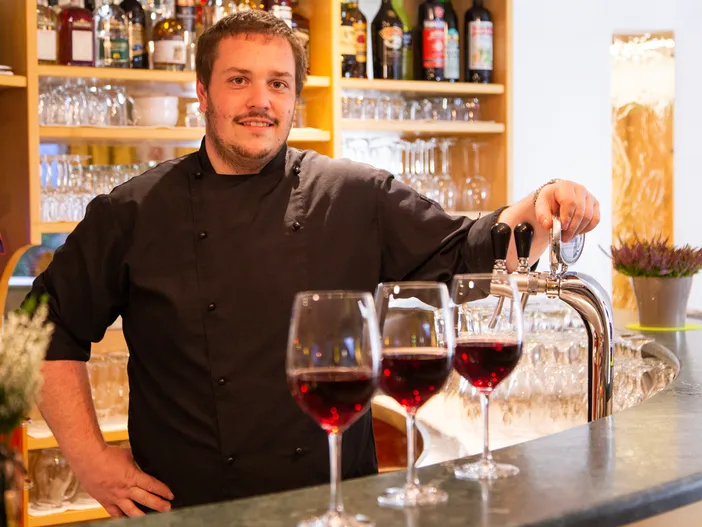 Lächelnder Barkeeper an der Theke mit drei Gläsern Rotwein und Zapfhahn
