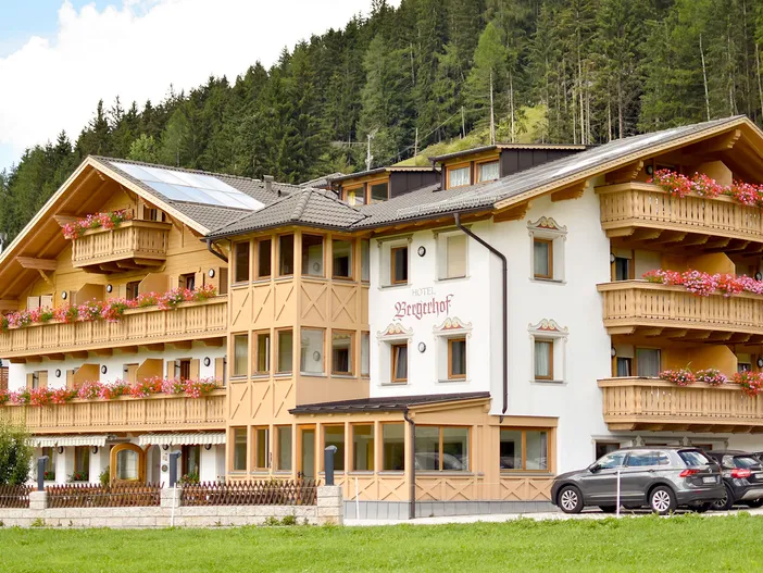 Almhotel Bergerhof mit Holzbalkonen und Blumenschmuck, umgeben von Bergwald, sonniger Tag