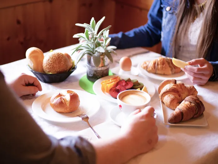 Frühstück zu zweit mit Croissants, Brötchen und Cappuccino in gemütlicher Südtiroler Holzstube