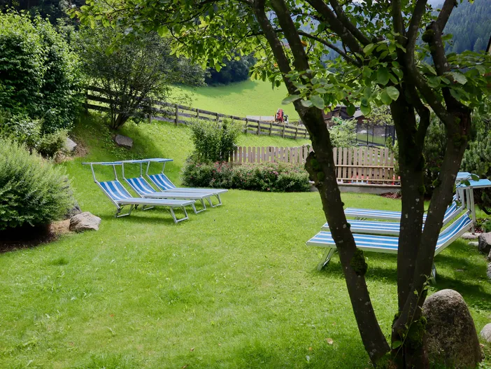 Liegestühle im grünen Hotelgarten unter schattigem Baum mit Blick auf Sarntaler Wiesen