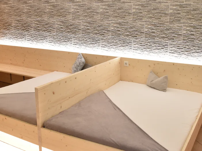 Ruhebett aus hellem Zirbenholz mit weichen Kissen und hinterleuchteter Natursteinwand