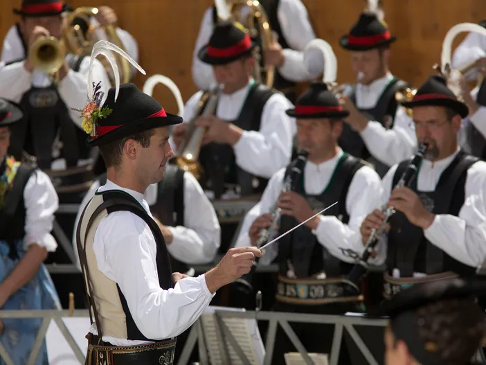 Kapellmeister in Tracht dirigiert Blasmusikkapelle bei sommerlichem Konzert im Sarntal