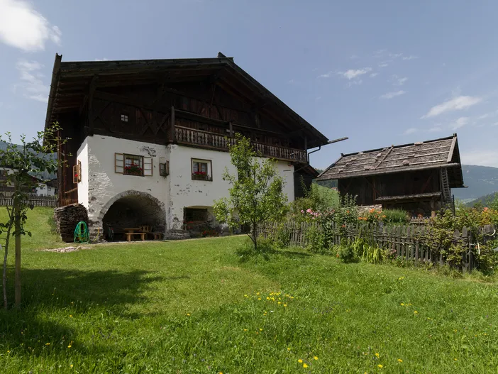 Historischer Südtiroler Bauernhof aus Holz und Stein mit blühendem Bauerngarten im Sommer