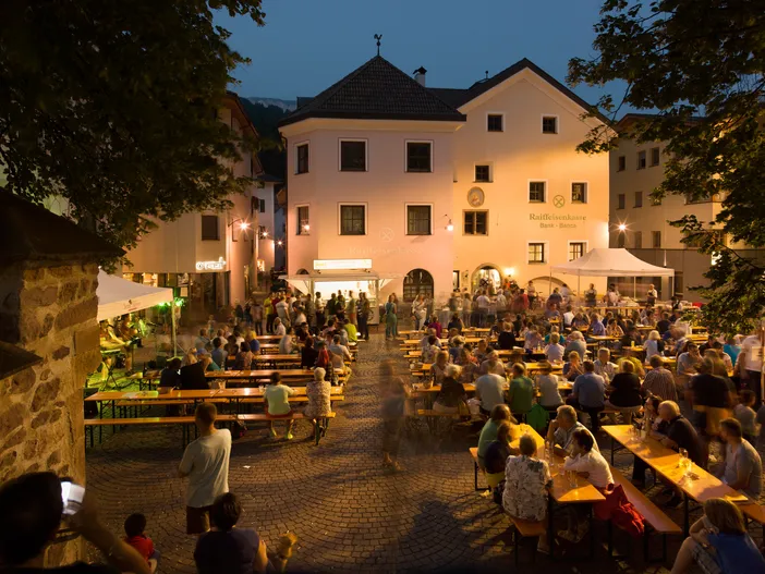 Belebtes Dorffest am Sarner Marktplatz mit Bierbänken und Besuchern in lauer Sommernacht