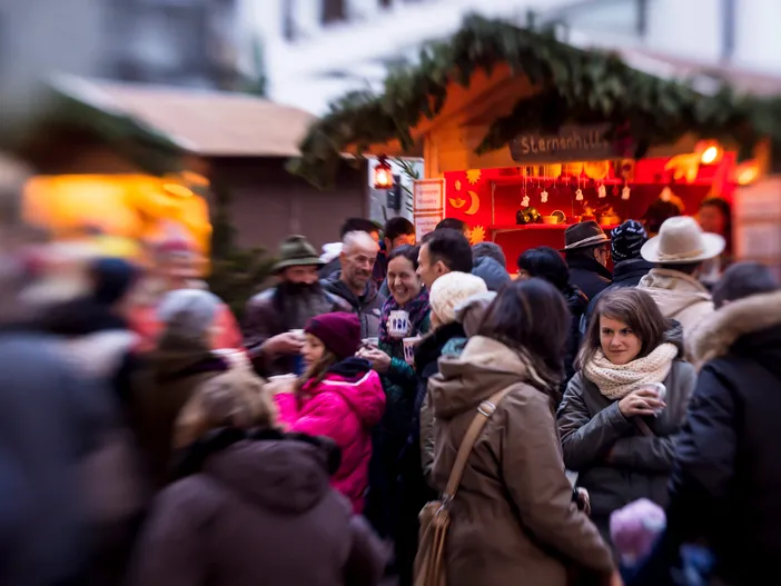 Fröhliche Menschen bei Glühwein an festlich geschmücktem Weihnachtsmarktstand in der Dämmerung
