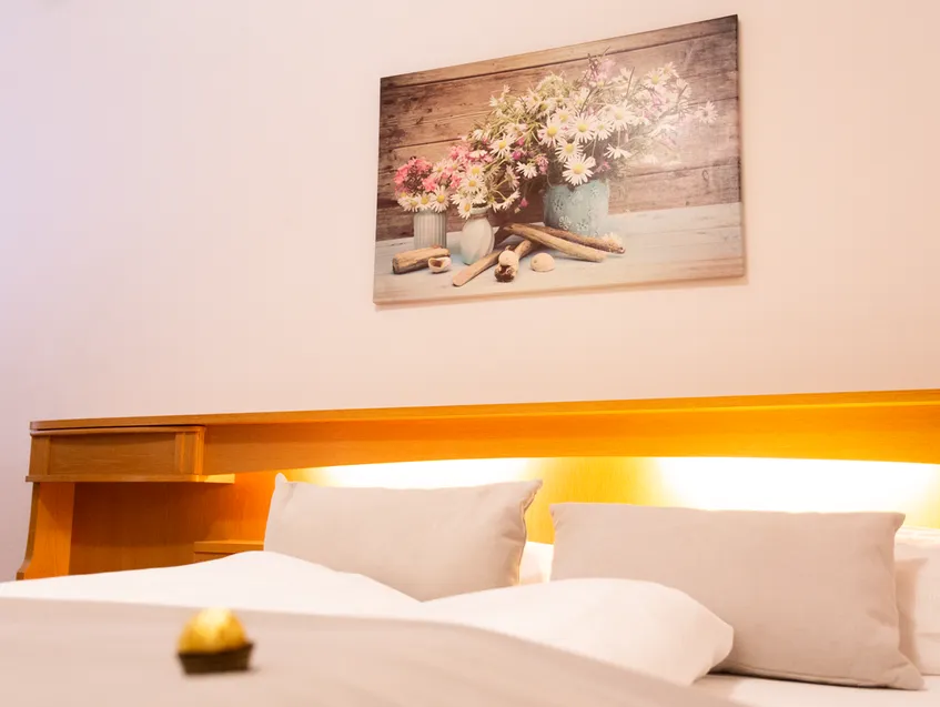 Doppelbett mit stimmungsvoller Beleuchtung am Holzkopfteil und Blumenbild an der Wand