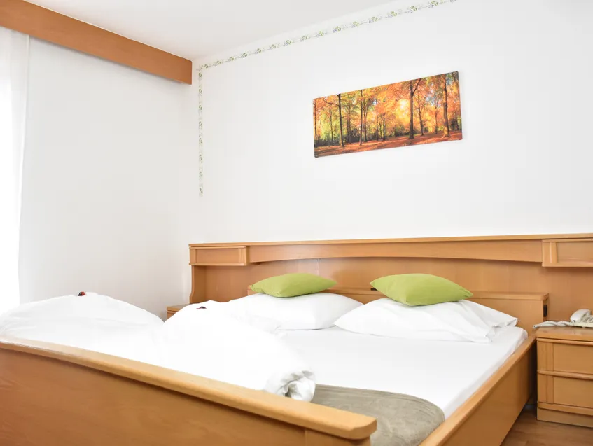 Doppelbett mit hellem Holzrahmen, integriertem Kopfteil und herbstlichem Waldmotiv