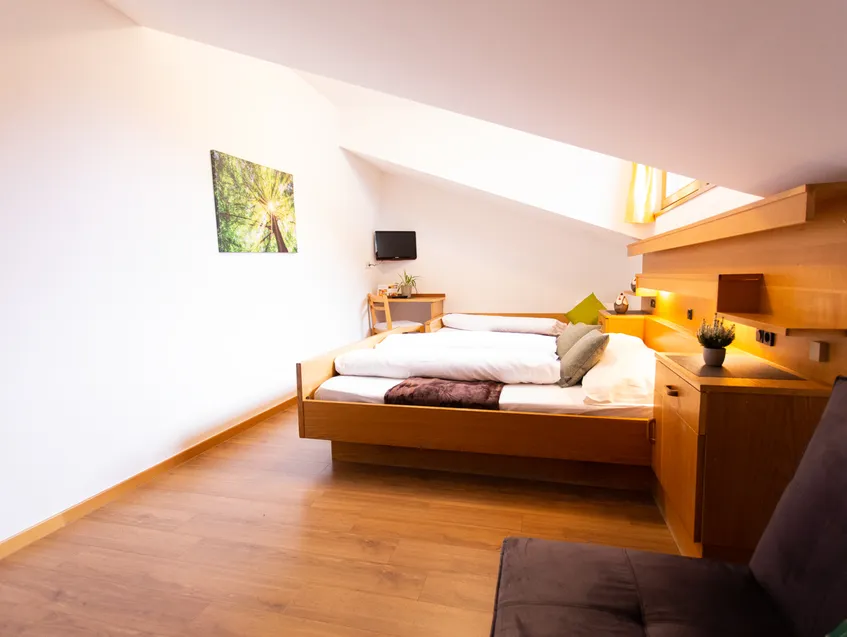 Helles Dachgeschosszimmer mit Doppelbett aus Holz, Dachschräge und Flachbild-TV