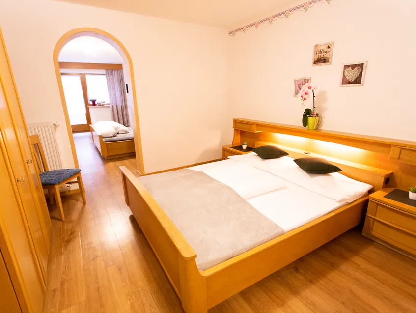 Doppelzimmer mit Holzbett und Durchgang zum Nebenraum im alpinen Stil