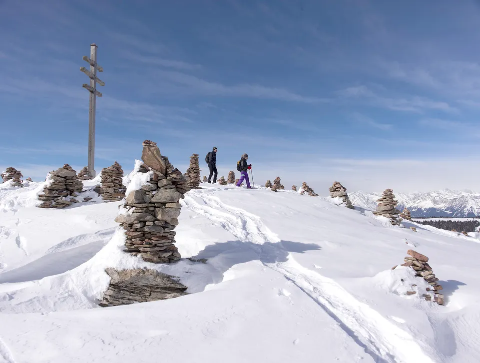 Zwei Skitourengeher zwischen schneebedeckten Steinmandln auf einem Gipfel der Sarntaler Alpen