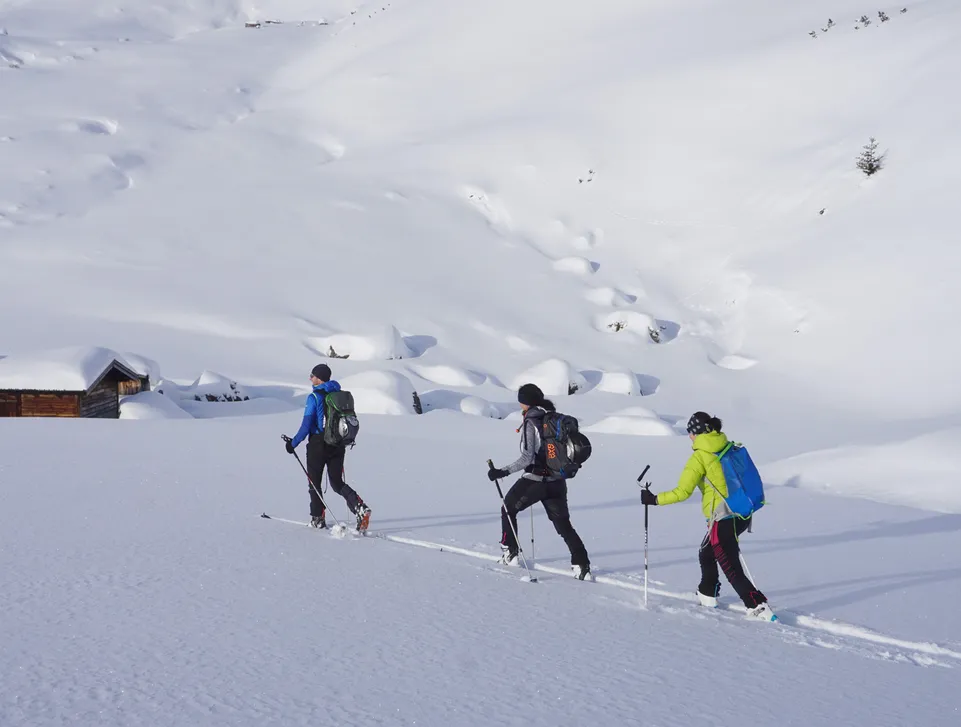 Drei Skitourengeher steigen im tiefen Schnee bei verschneiter Almhütte im Sarntal auf