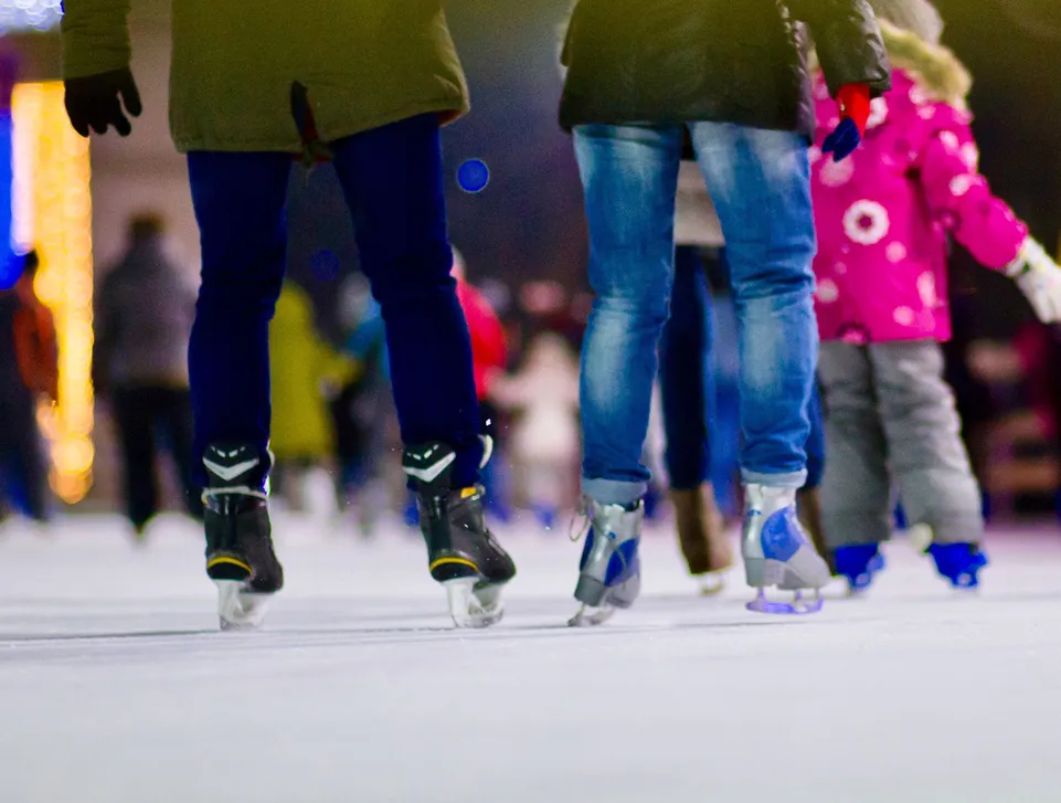 Familie beim abendlichen Eislaufen auf beleuchteter Eisbahn im winterlichen Sarntal