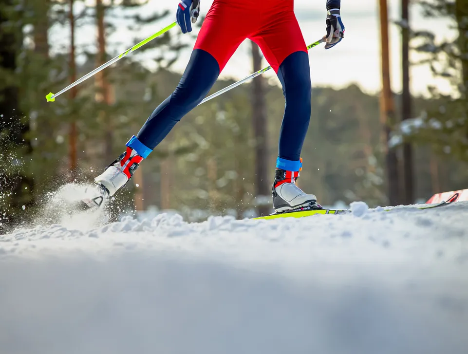 Langläufer in roter Sportkleidung auf verschneiter Loipe durch Winterwald im Sonnenlicht