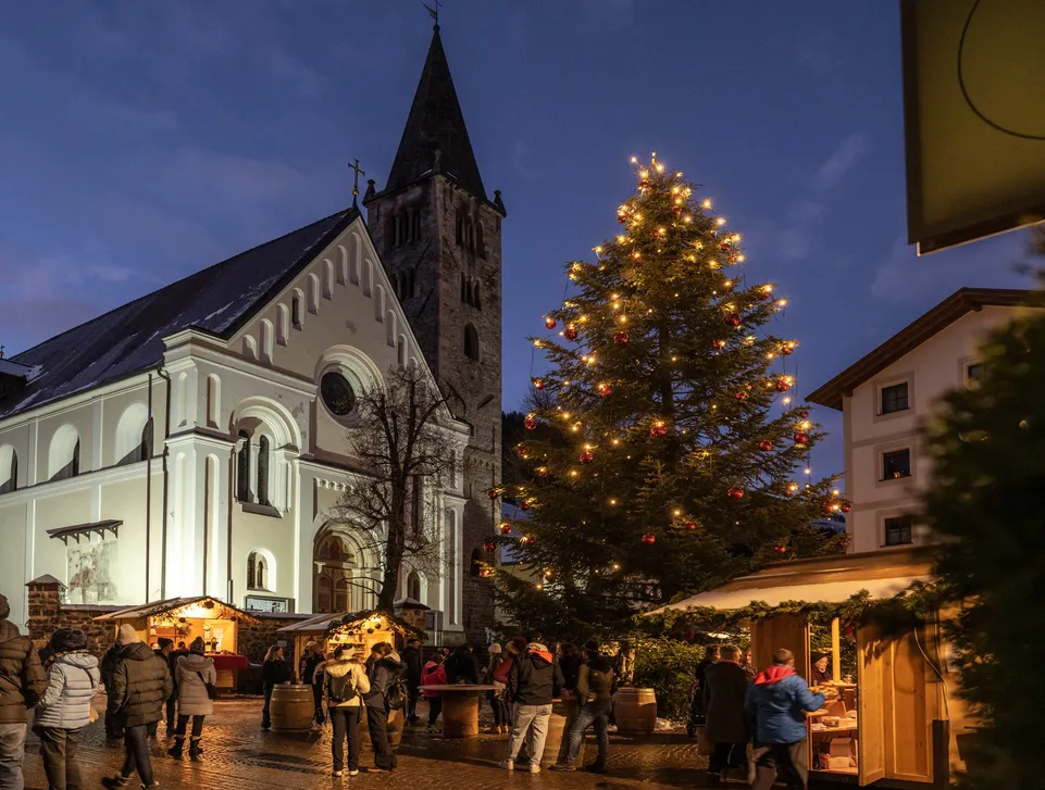 Weihnachtsmarkt mit beleuchtetem Christbaum vor der Sarner Kirche in der blauen Abendstunde