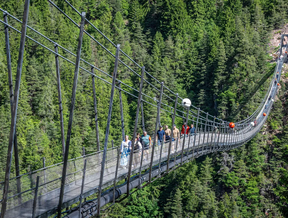 Wanderer überqueren die Hängebrücke über die bewaldete Schlucht im Sarntal im Sommer