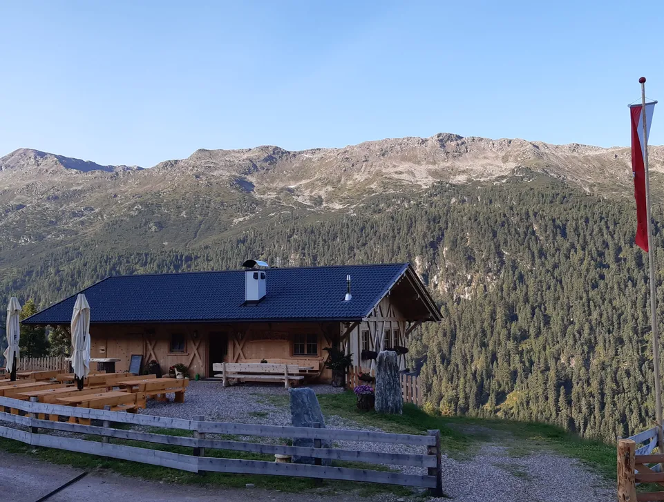 Gemütliche Almhütte mit Sitzbänken und Südtiroler Fahne vor bewaldeten Bergen im Herbst