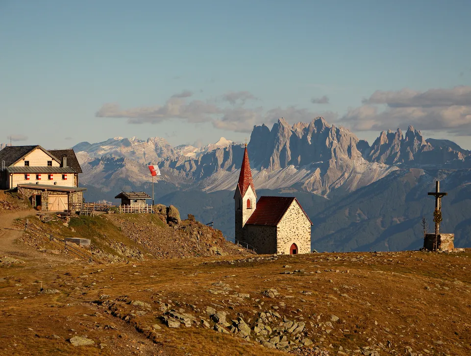 Latzfonser Kreuz mit Schutzhütte und Bergkapelle vor Dolomitenpanorama im Abendlicht