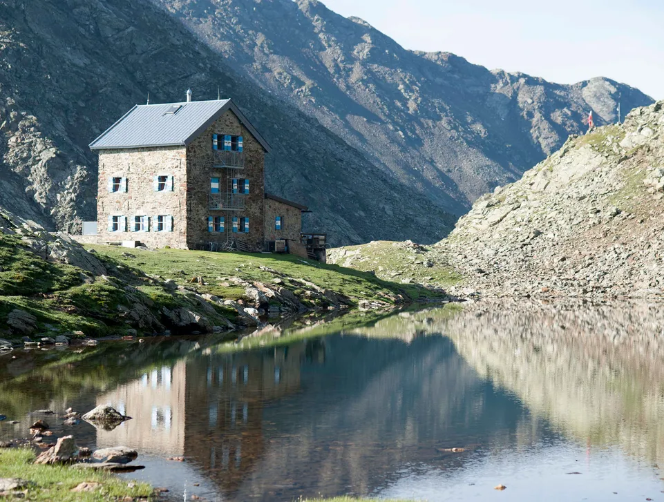 Steinerne Almhütte am spiegelglatten Bergsee inmitten schroffer Felsberge in Südtirol