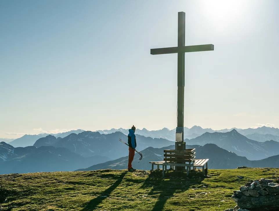 Wanderer am Gipfelkreuz genießt den weiten Blick über die Südtiroler Bergketten